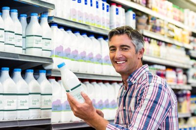 Mann mittleren Alters steht vor einem Milchregal im Supermarkt und freut sich, dass er das Etikett ohne Lesebrille erkennen kann.